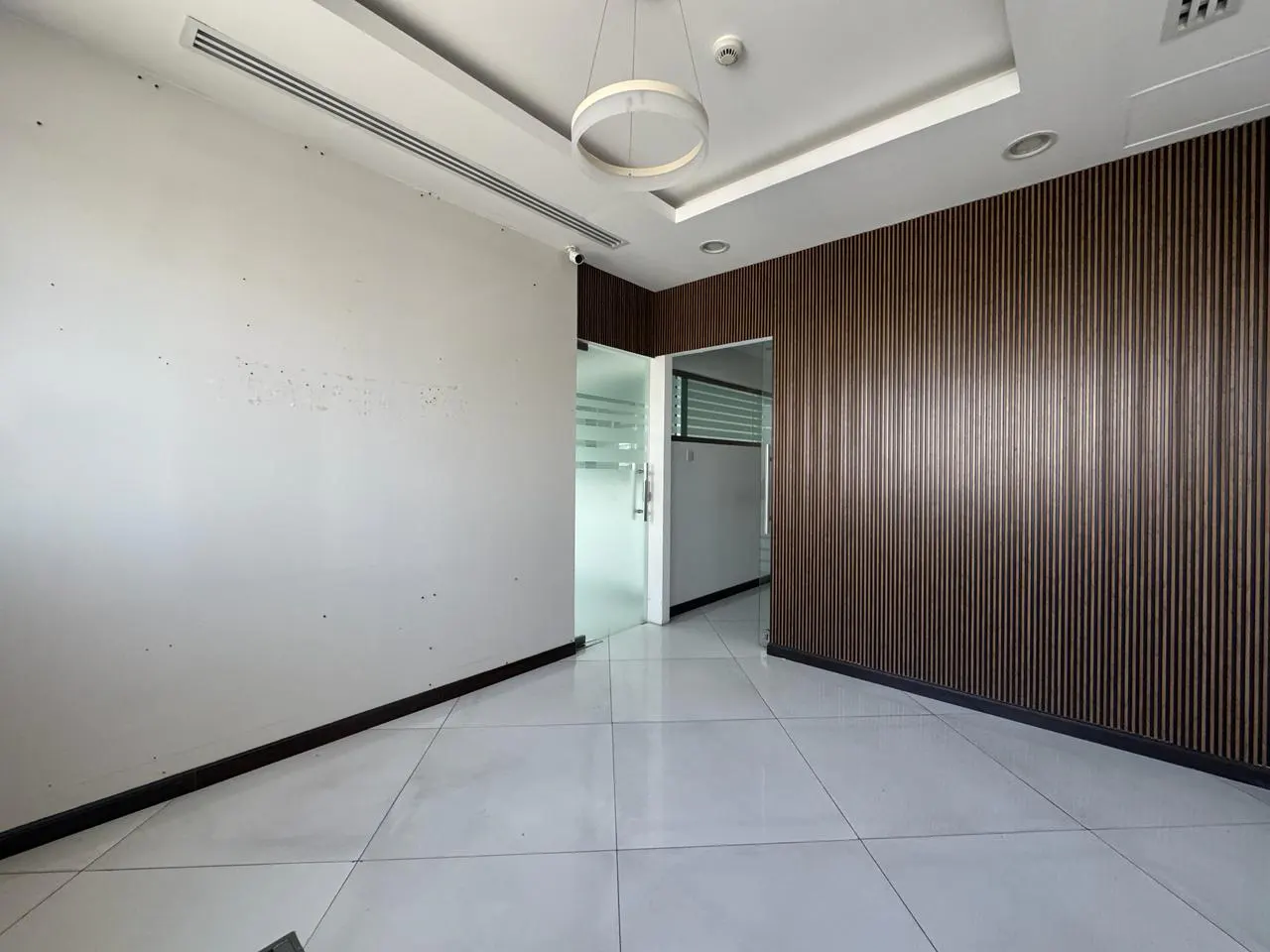 Modern office interior with white walls, a dark wood-slatted accent wall, white tile floors, and a glass door entrance.