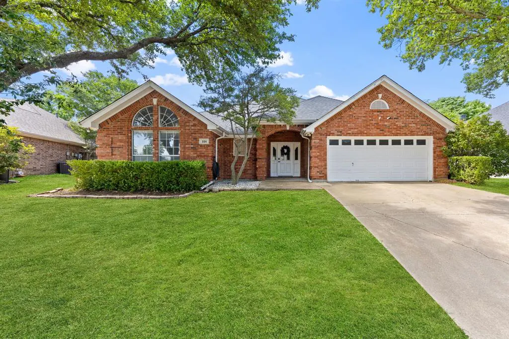 Red brick house with a white garage door and front door, green lawn, and trees under a blue sky.