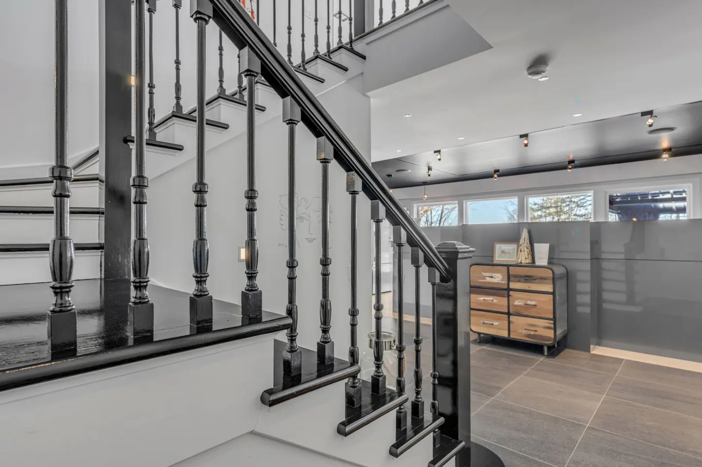 Interior view of a staircase with black banister and white walls, leading to a tiled floor and a wooden cabinet.