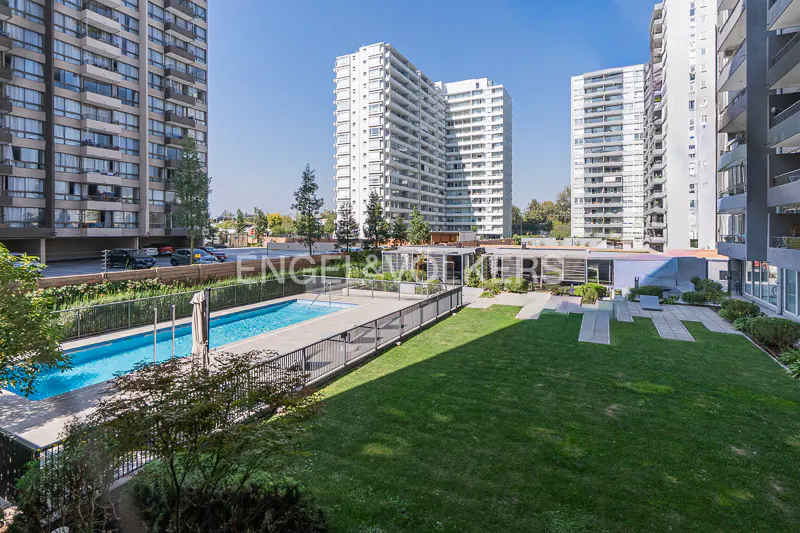 Apartment complex with a pool and green space. Tall buildings surround the area under a clear blue sky.