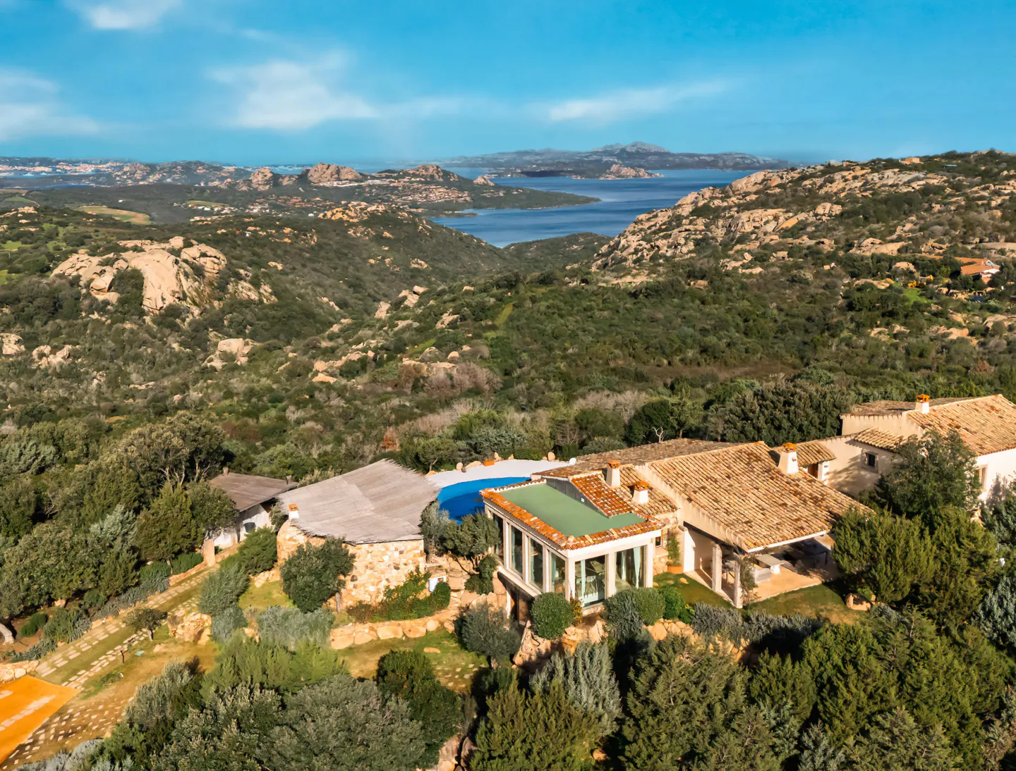 Aerial view of a luxury home with a pool, surrounded by green hills and a blue sea in the background.