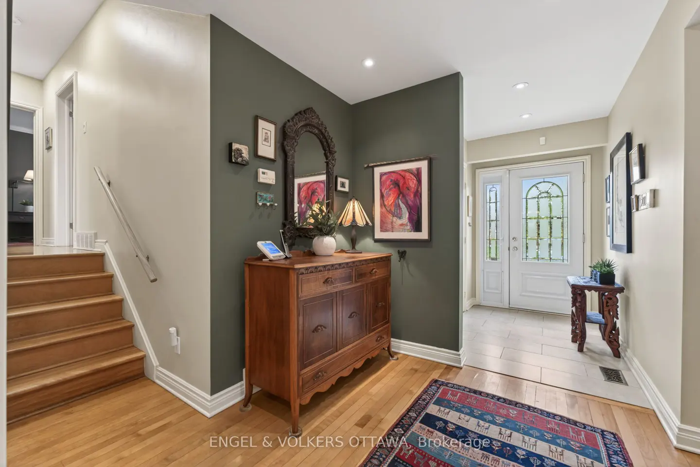 Foyer with wooden floors, stairs, and a green accent wall. A wooden dresser with a mirror and artwork sits against the wall. A white front door is visible.