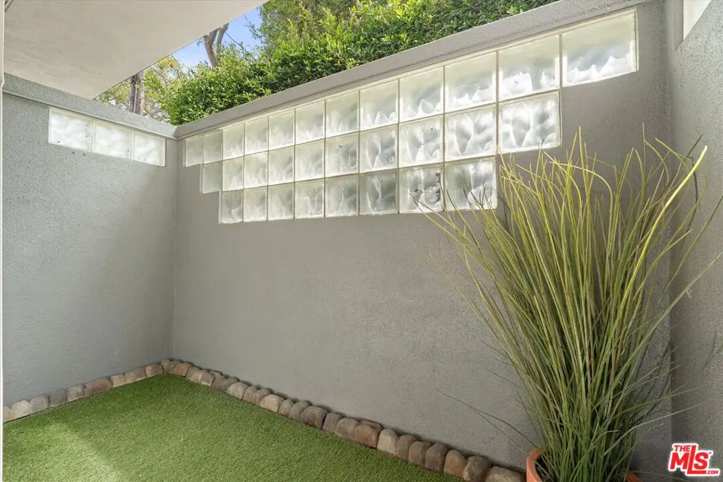 A small outdoor patio with a glass block wall, artificial turf, and a potted plant.