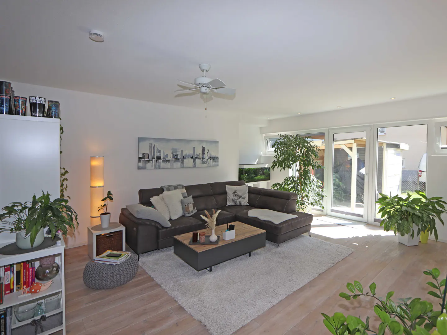 Modern living room with a grey sectional sofa, wooden coffee table, white rug, and large glass doors leading to a patio.