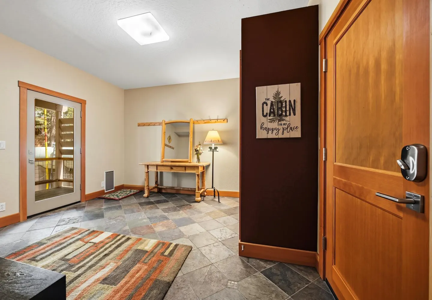 Entryway with slate tile floor, wooden console table, mirror, floor lamp, and a sign reading "The Cabin is my happy place."