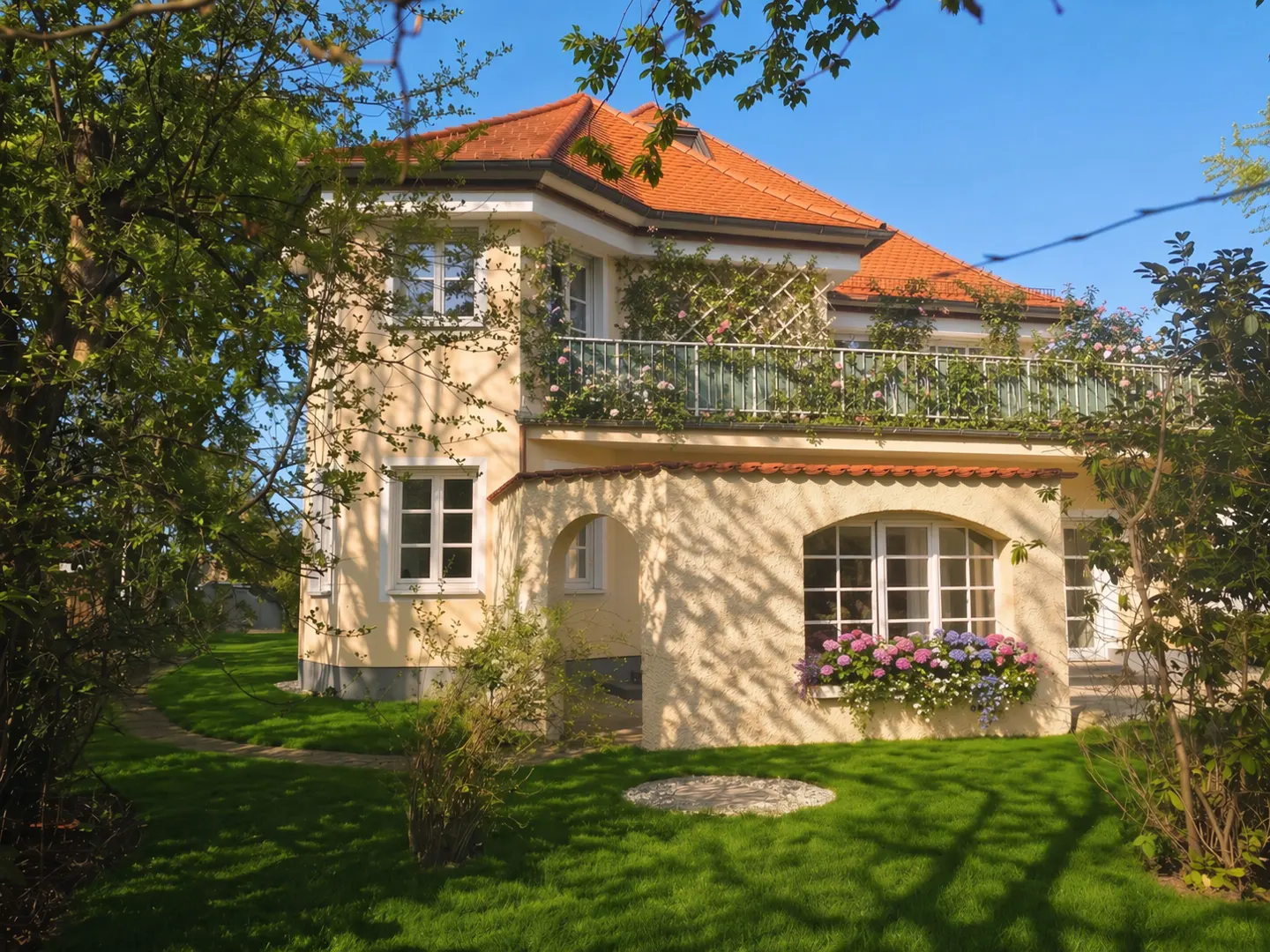 Two-story house with orange roof, beige walls, white windows, and a balcony with flowers. Green lawn and trees surround the house.