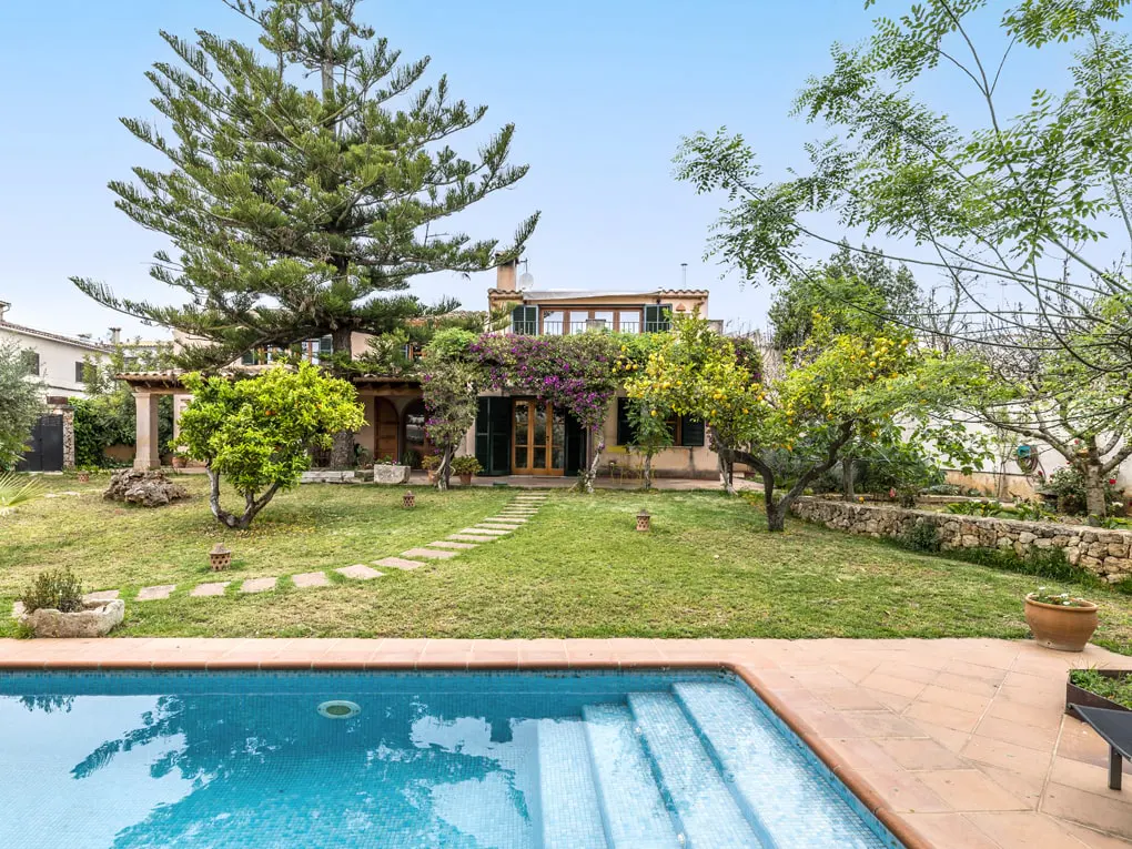 Backyard view of a two-story house with a pool, lawn, trees, and stone pathway. The pool has blue water and tile steps.