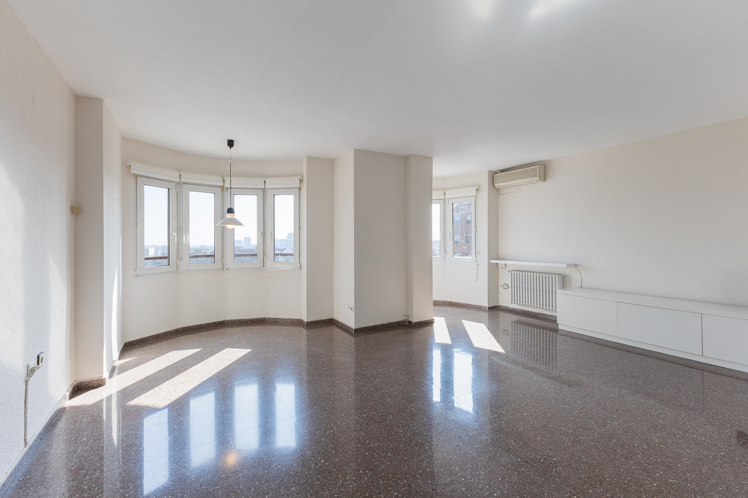 Bright, empty living room with white walls, polished dark stone floors, a bay window, and a modern white cabinet.