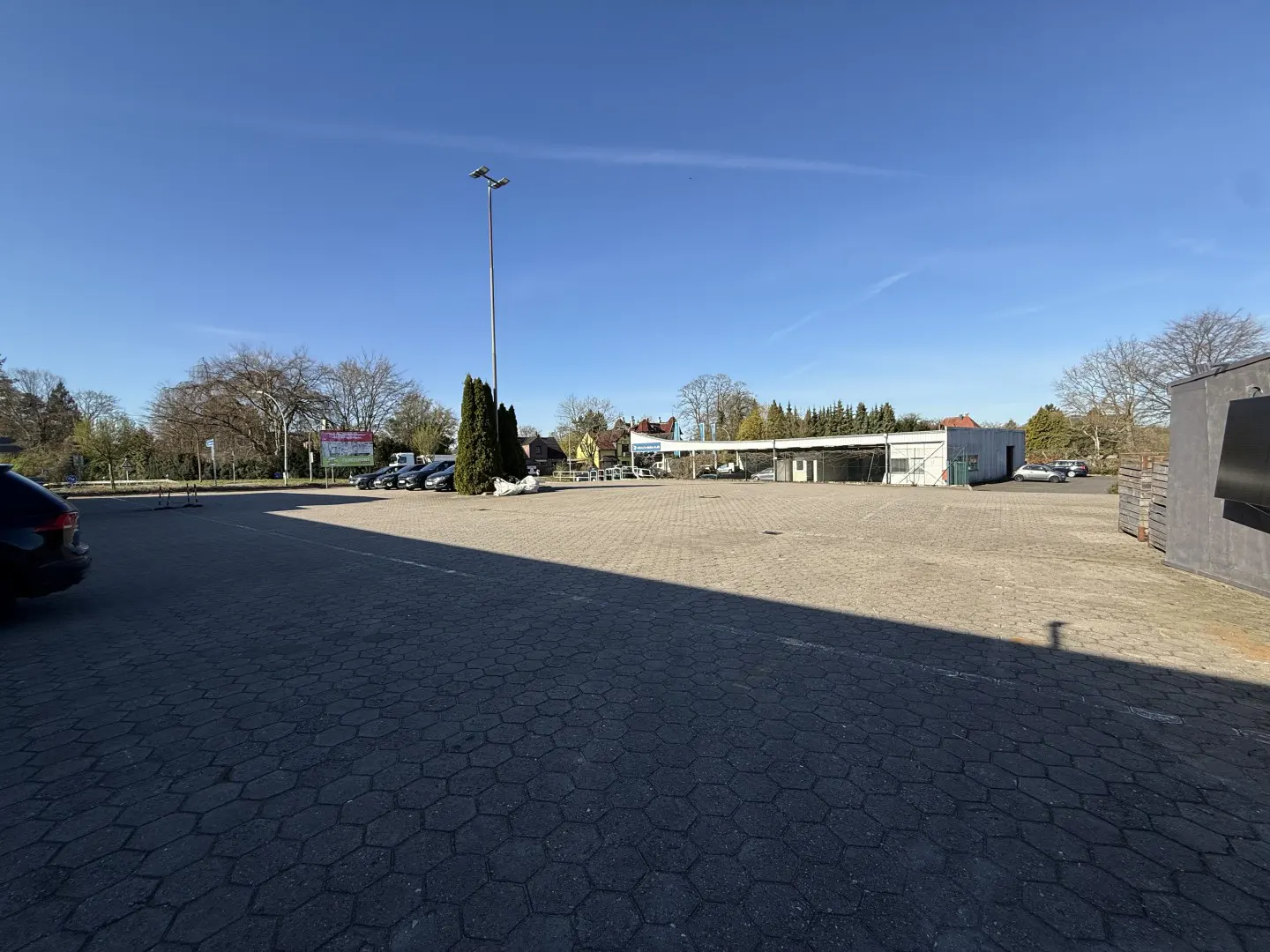 A wide shot of a large, empty parking lot with a building in the background on a sunny day.