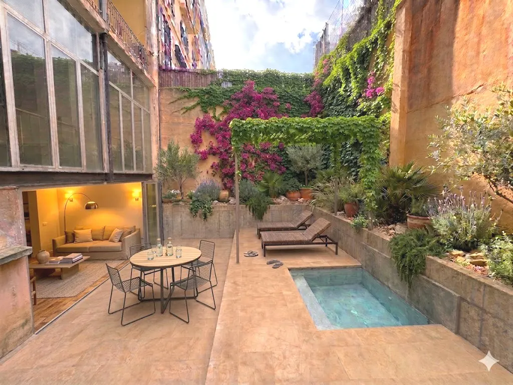 Private courtyard with a small pool, lounge chairs, dining set, and lush greenery against a tall, vine-covered wall.