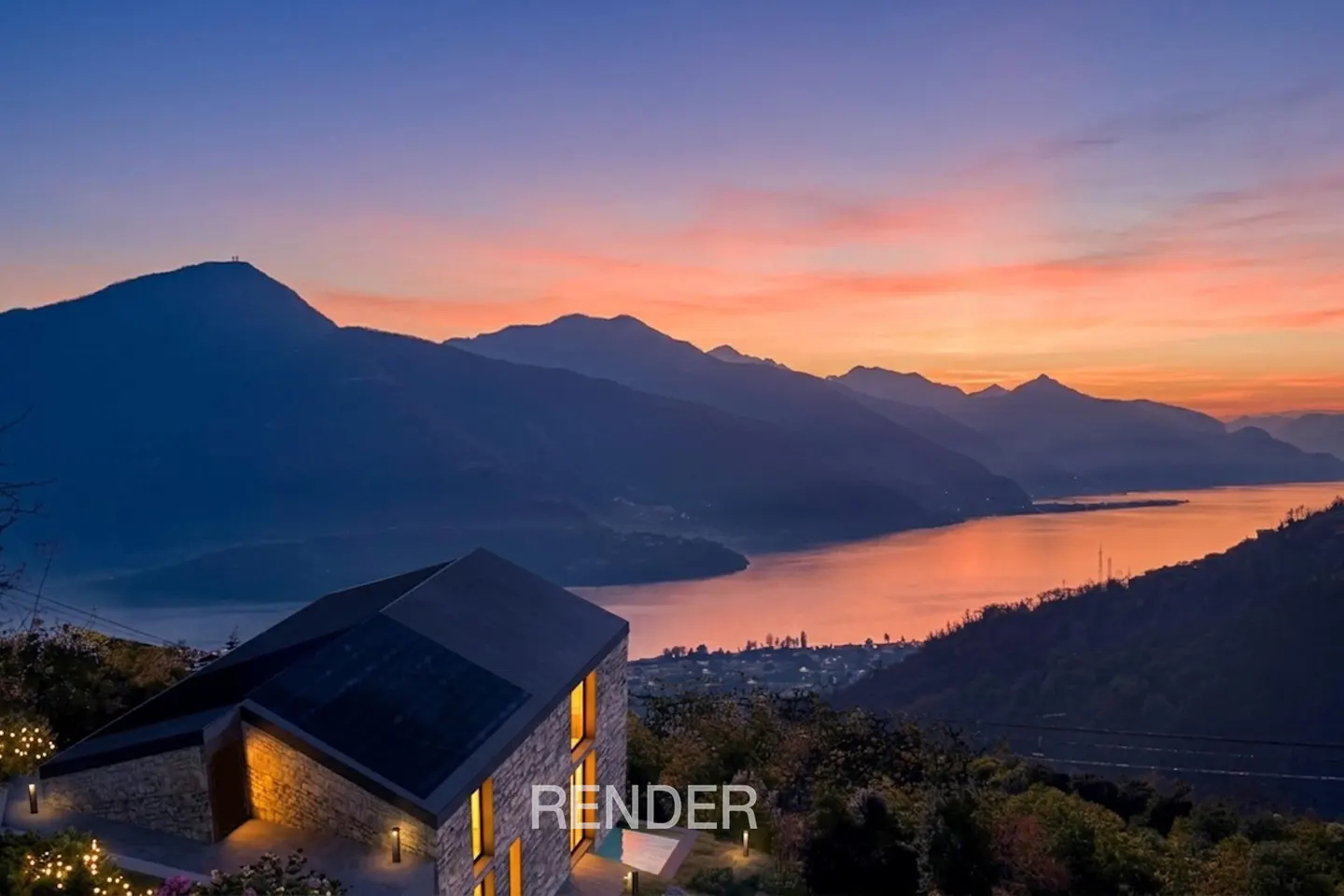 Modern stone house with warm interior lighting overlooking a lake and mountain range at sunset.