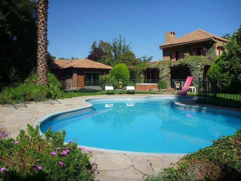 A backyard with a blue pool, stone patio, lounge chairs, and a house with a red slide.