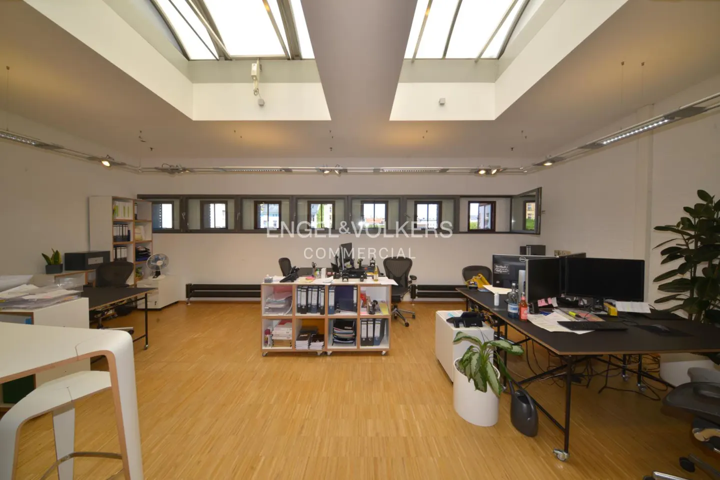Bright office space with skylights, desks, and wood floors. Engel & Volkers Commercial logo visible.