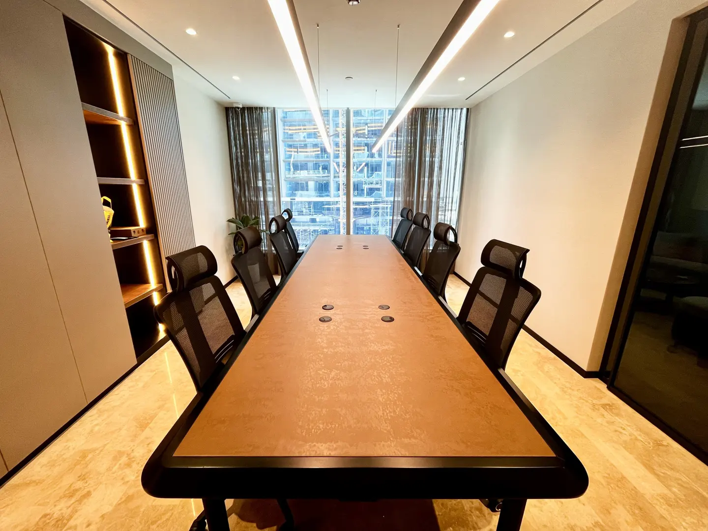 A modern conference room with a long brown table, black mesh chairs, and a large window overlooking a city skyline.