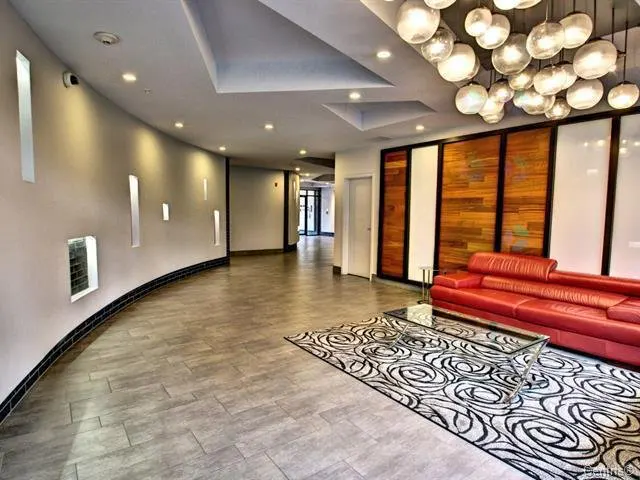 A modern lobby with a red leather sofa, glass table, and patterned rug. The walls are curved with recessed lighting and decorative niches.