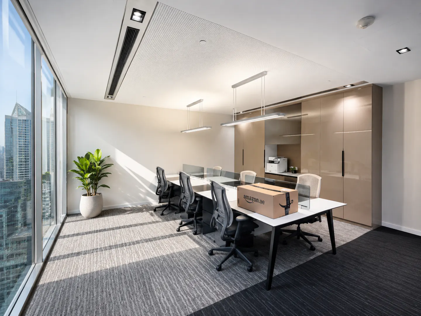 Modern office with a long desk, ergonomic chairs, a potted plant, and an Amazon package, overlooking a city skyline.