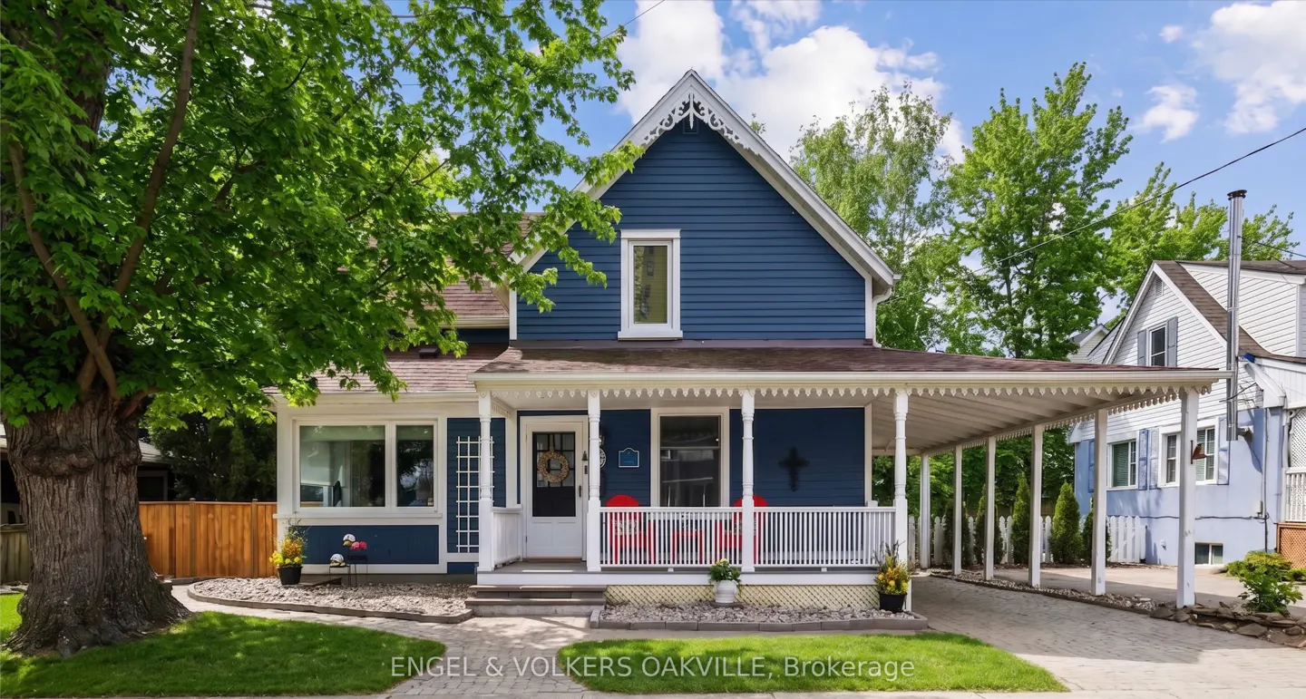 Two-story blue house with white trim, a covered porch, and a driveway. A large tree is on the left side of the house.