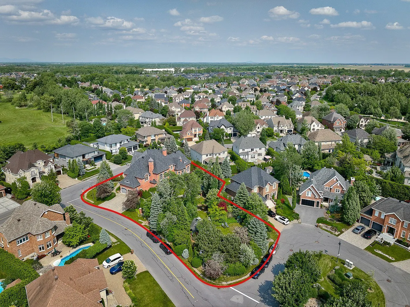Aerial view of a large brick house with a red outline, surrounded by trees and other houses in a suburban neighborhood.