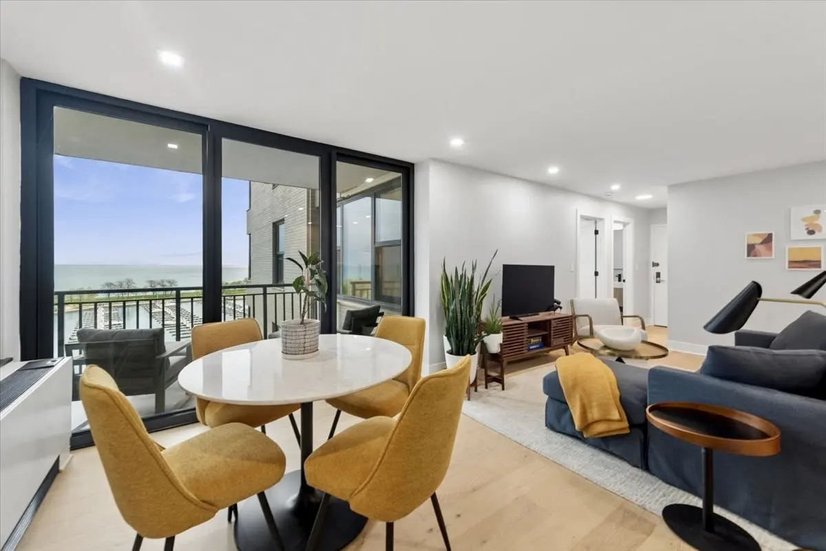 Bright living space with a round white table, yellow chairs, and a blue sofa. Large windows offer a view of the lake.