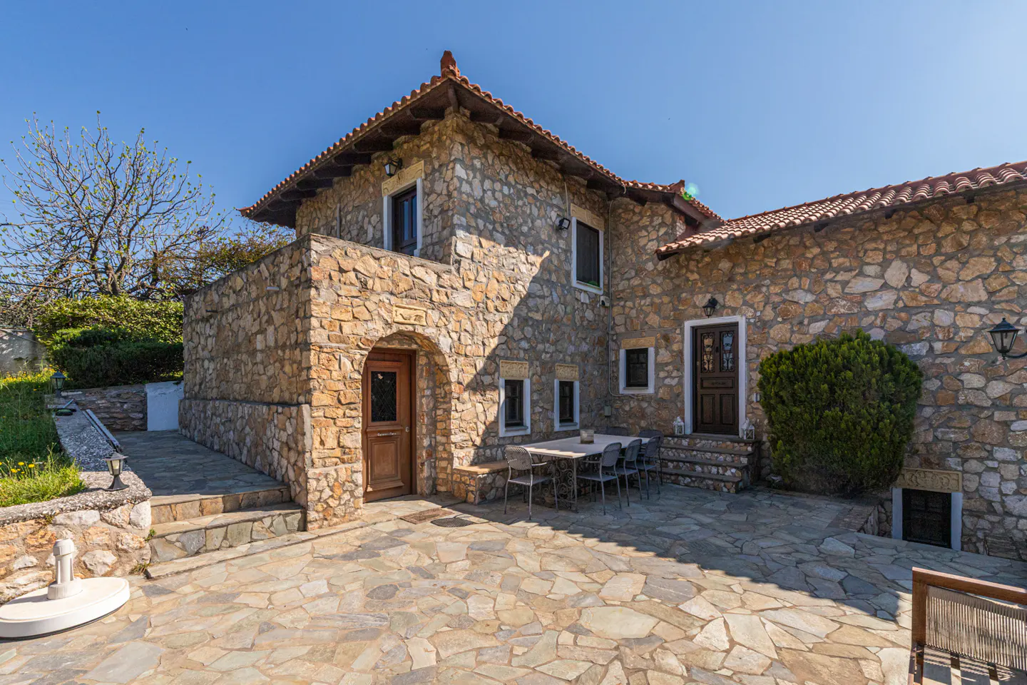 Stone house with a brown tile roof, a stone patio, and an outdoor dining table with chairs.