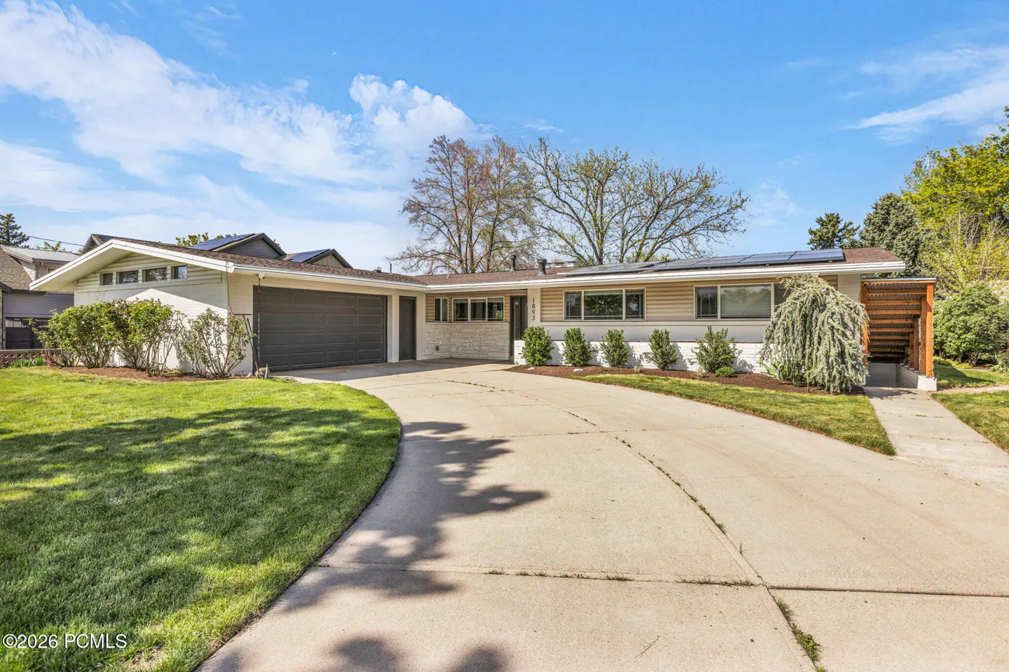 A single-story house with a gray garage door, a concrete driveway, and solar panels on the roof.