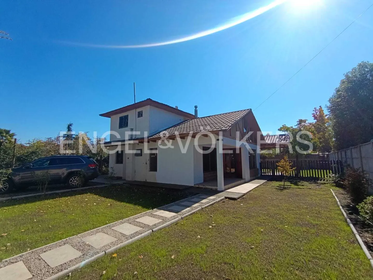 Two-story white house with a brown roof, green lawn, and a car parked in the driveway under a clear blue sky.