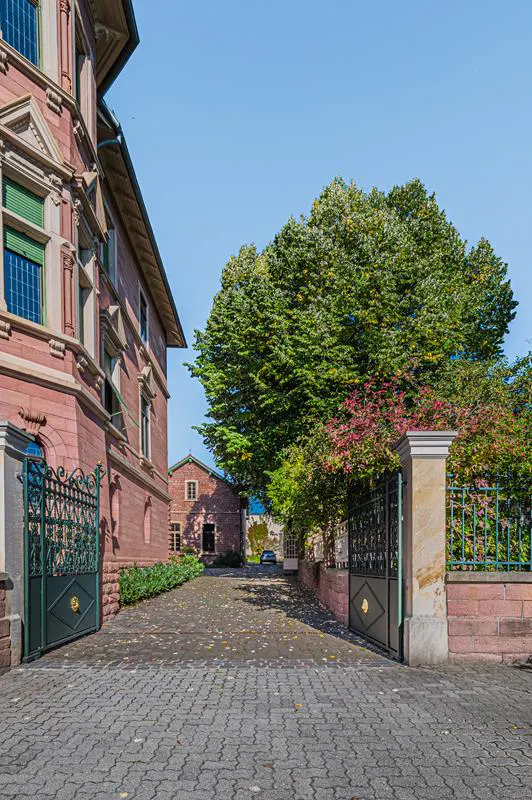 Exterior view of a red brick building with green shutters and a gated entrance on a cobblestone driveway.