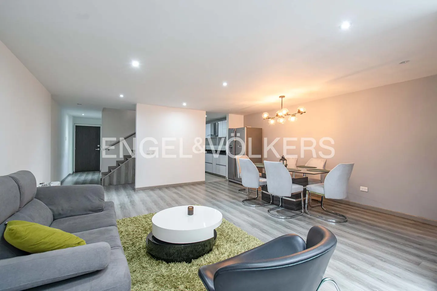 Open-concept living and dining area with gray sofa, round coffee table, and dining set under a modern chandelier.
