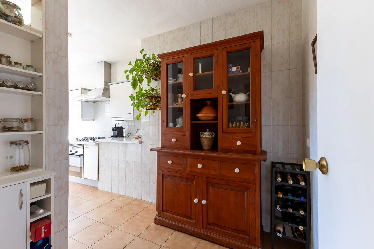 A kitchen with a large, dark wood hutch, a wine rack, and a view into a white kitchen.