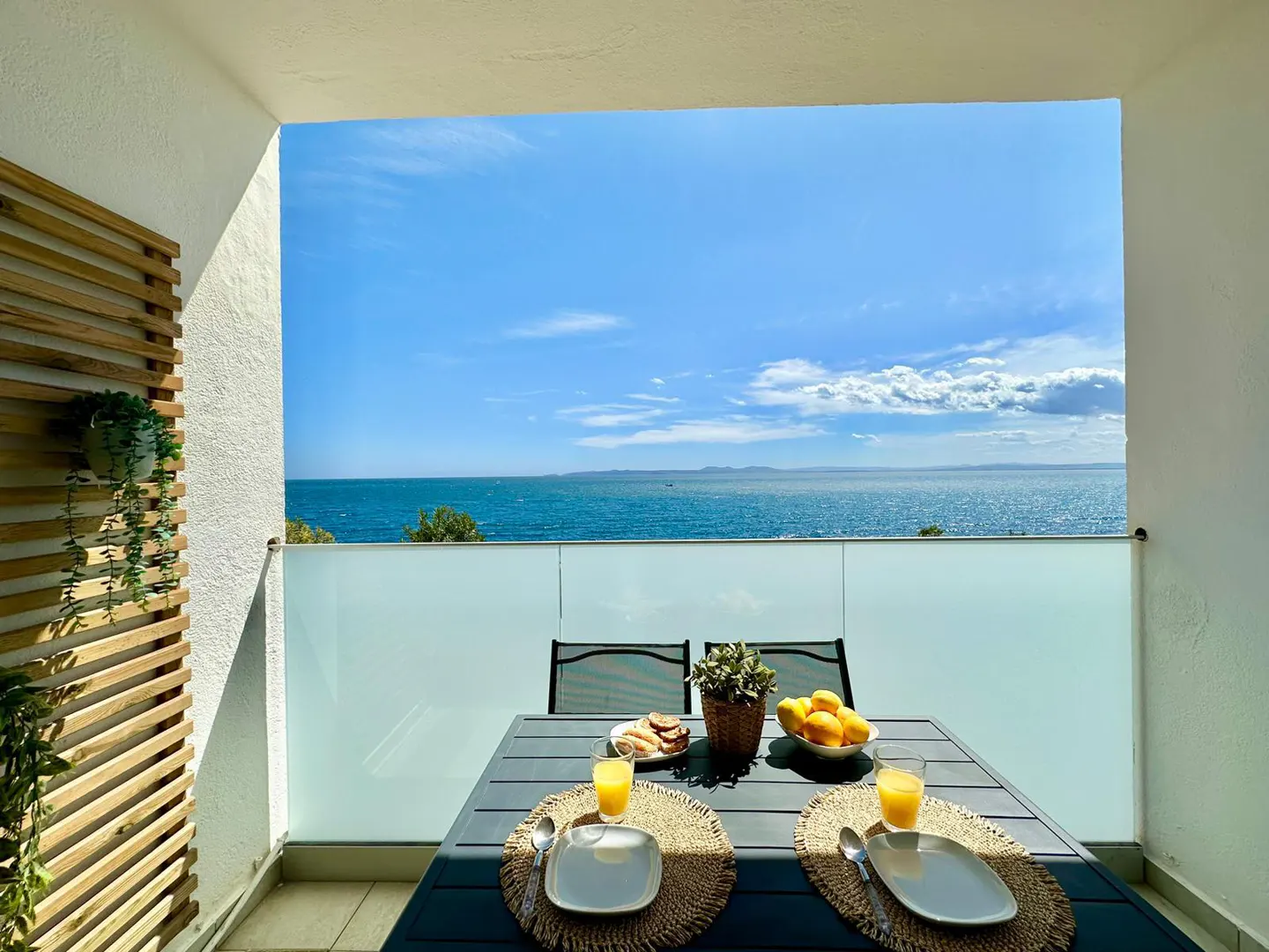 Balcony with a table set for breakfast overlooking the ocean on a sunny day.