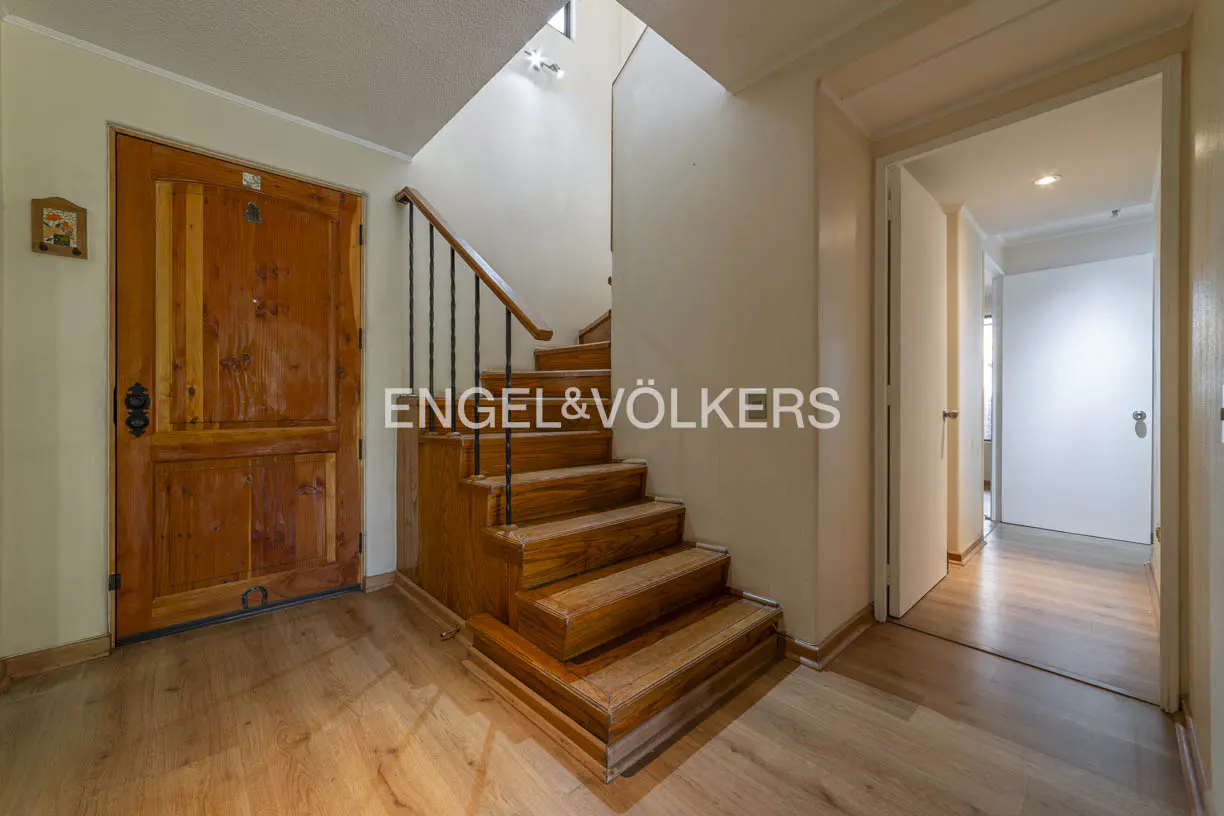 Interior view of a home featuring a wooden door, staircase with black railing, and hallway leading to another room.