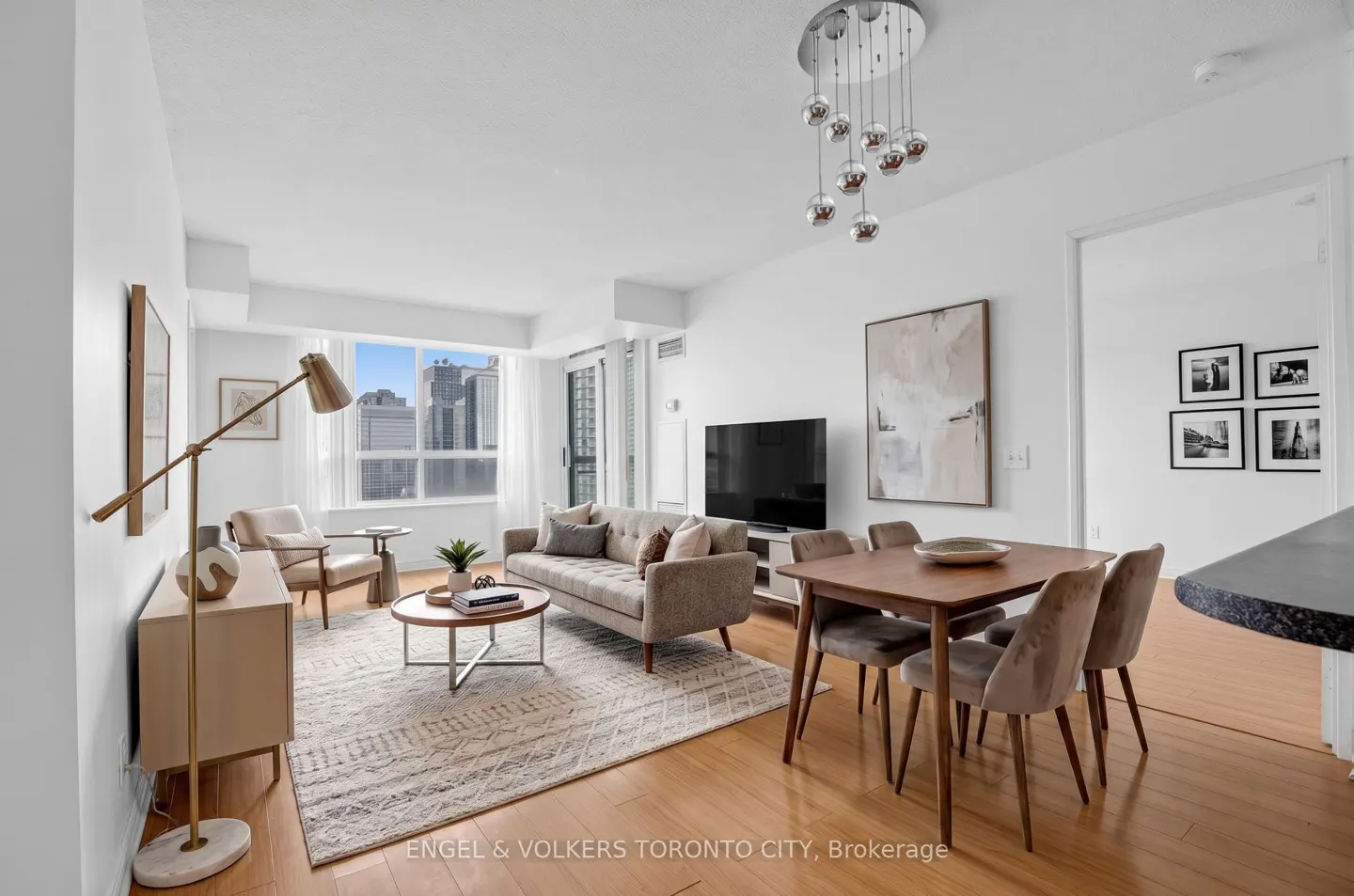 Bright, modern condo living room with a beige sofa, wood dining table, and city views from the window.