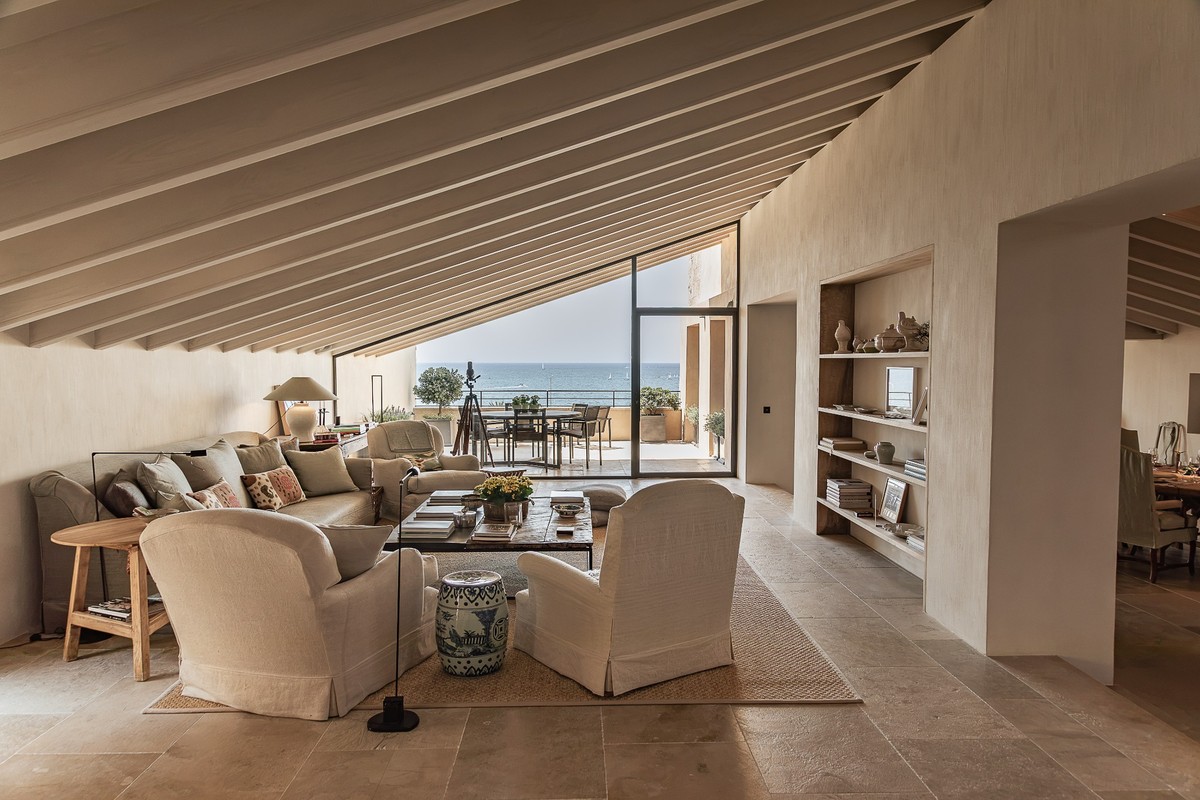 Neutral-toned living room with sloped ceiling, white armchairs, coffee table, and a balcony overlooking the ocean. [AI-generated text]