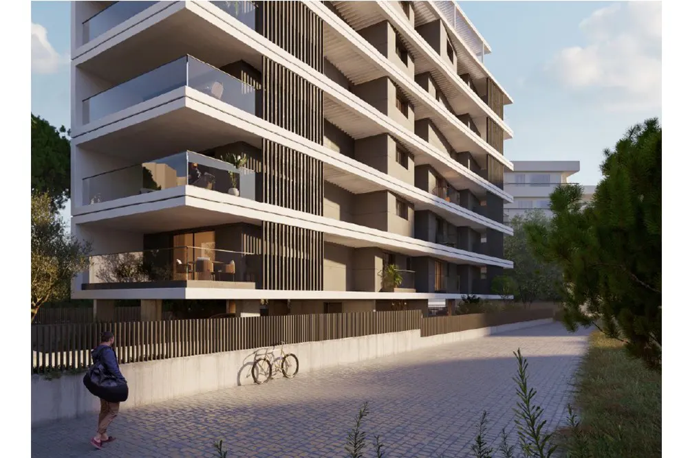 Modern apartment building with balconies and glass railings. A person walks by two bicycles parked near a fence.
