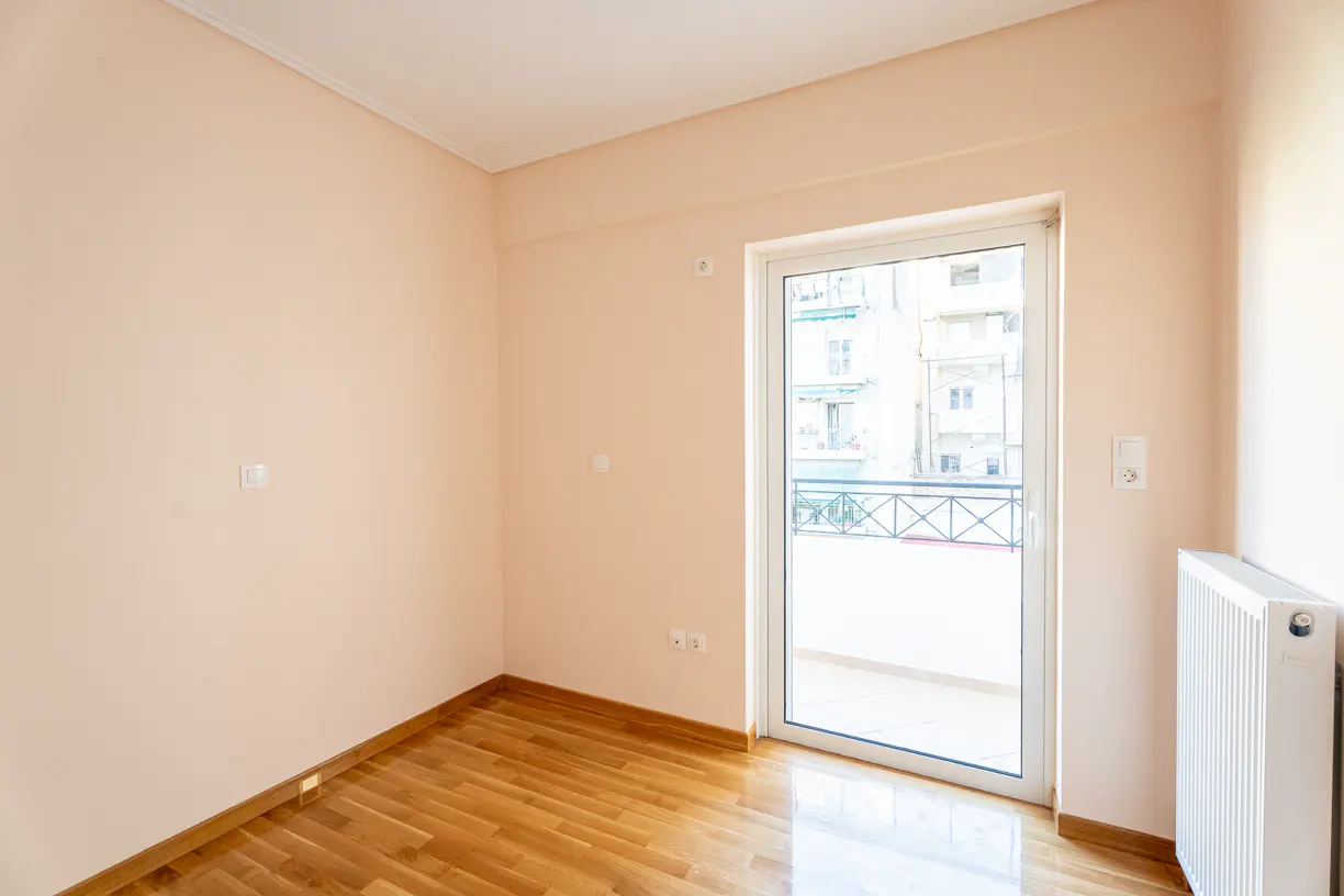 Empty room with peach walls, wood floors, and a white sliding glass door to a balcony. A white radiator is on the right wall.