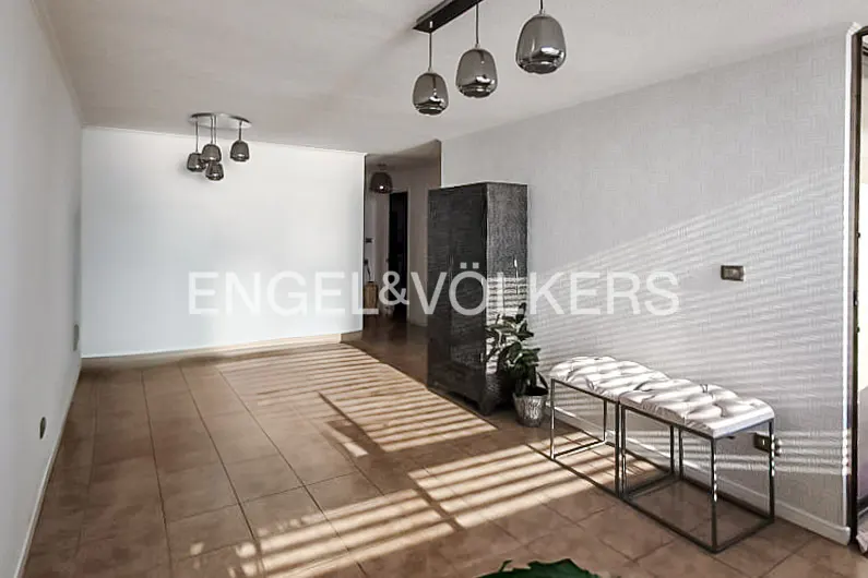 Bright living area with tiled floors, modern pendant lights, a dark cabinet, and a white bench under sunlight.