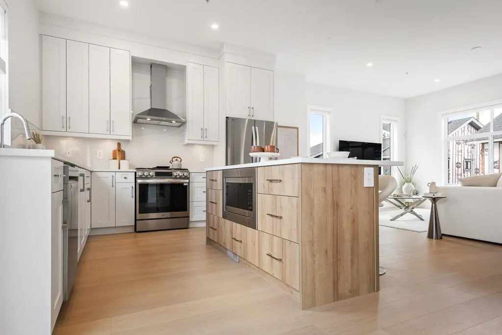 Bright, modern kitchen with white cabinets, stainless steel appliances, and a wood-paneled island. Living room visible in the background.