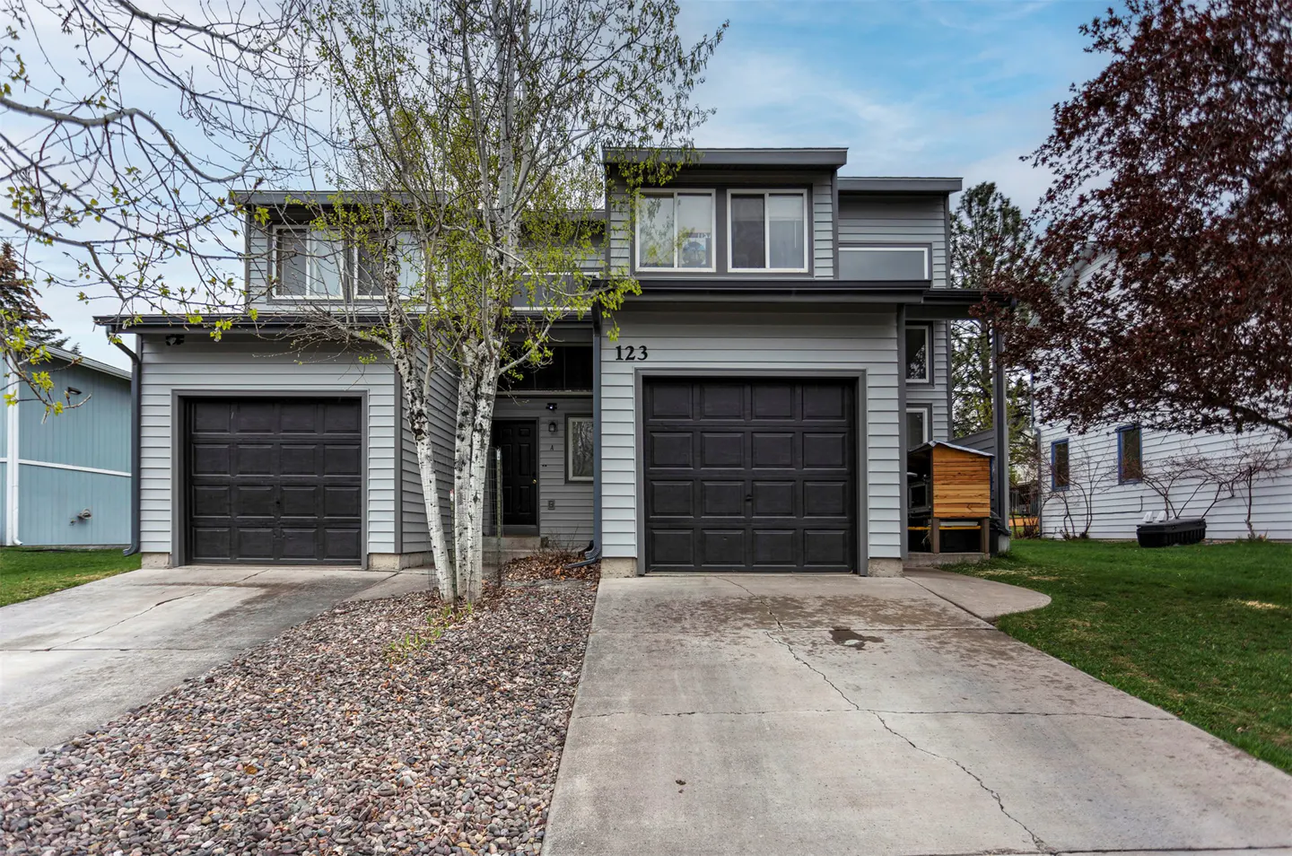 Gray townhouse with two black garage doors and the number 123 above the right garage. A concrete driveway leads to the street.