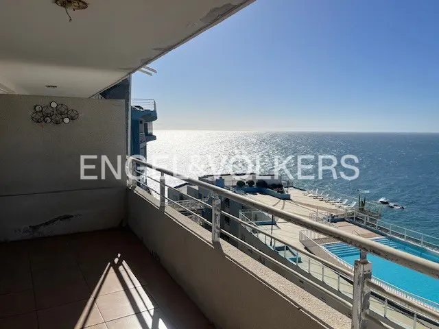 View from a balcony overlooking the ocean, a pool, and lounge chairs on a sunny day.
