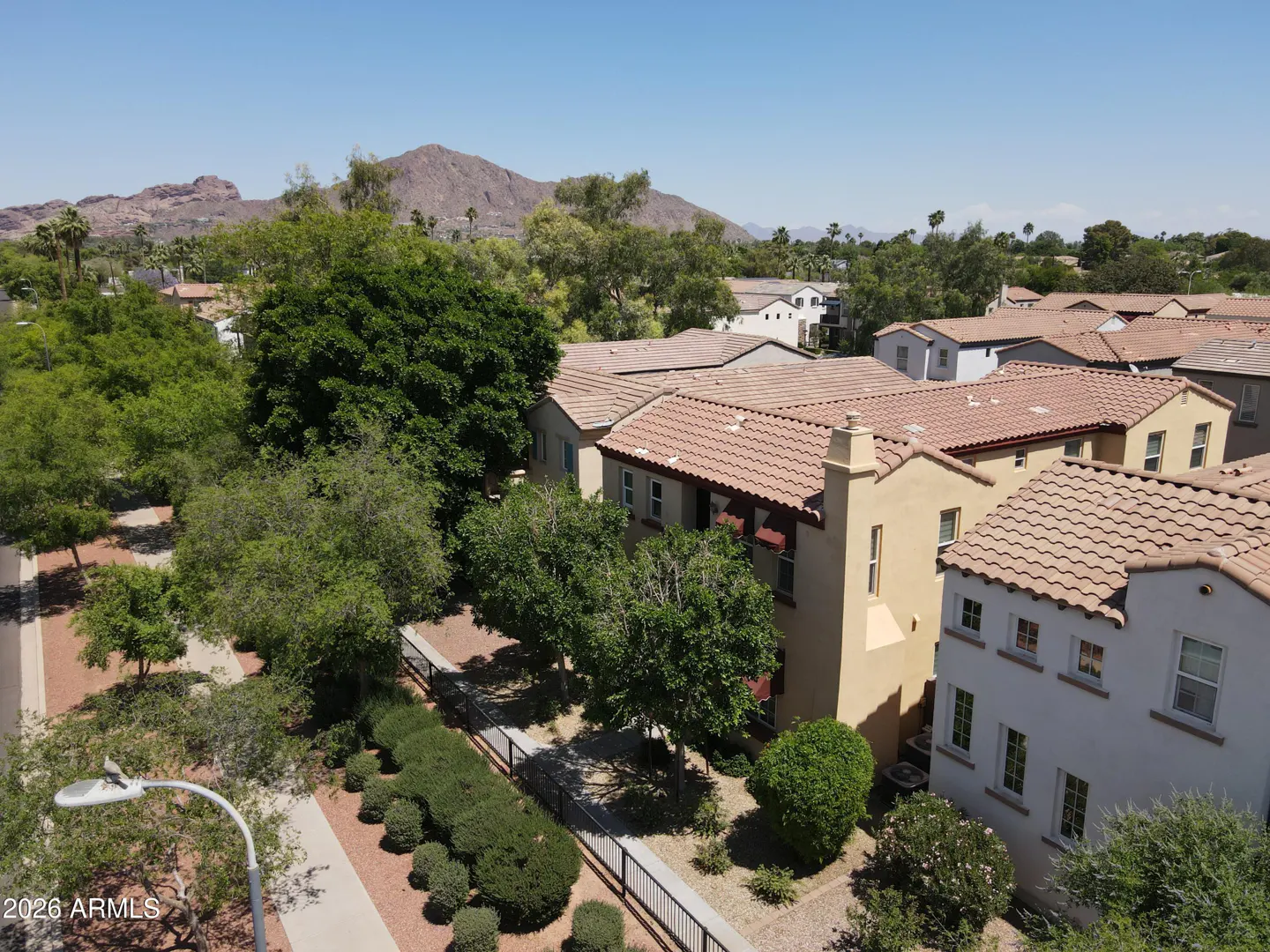 Aerial view of tan and white townhouses with red tile roofs, green trees, and a mountain in the background.