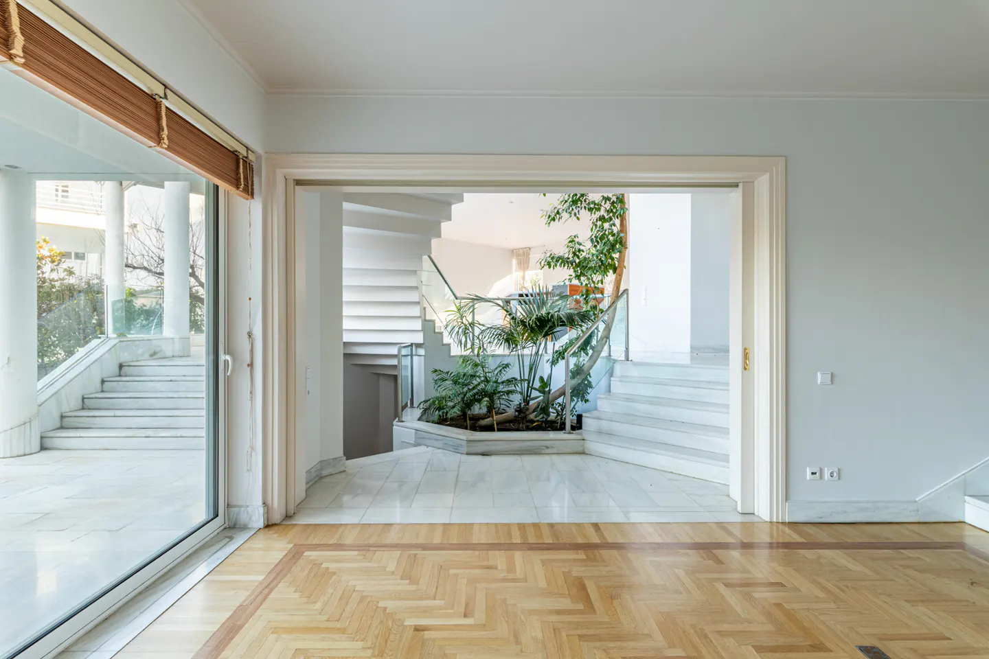 Interior view of a home with herringbone wood floors, marble stairs, and a plant display. A sliding glass door leads to an outdoor staircase.
