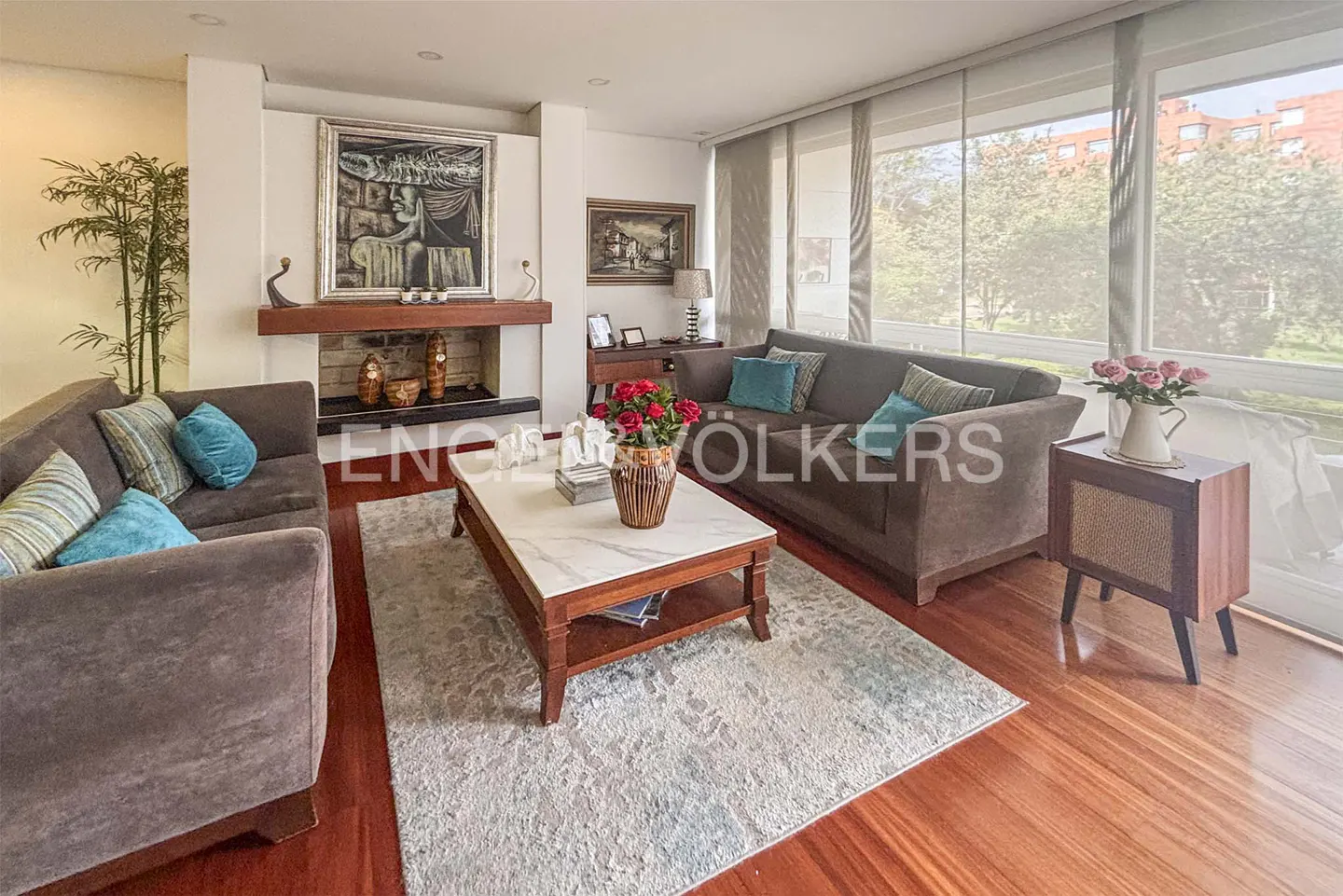 Living room with brown sofas, a marble-top coffee table, and a fireplace with art above. Large windows offer natural light.