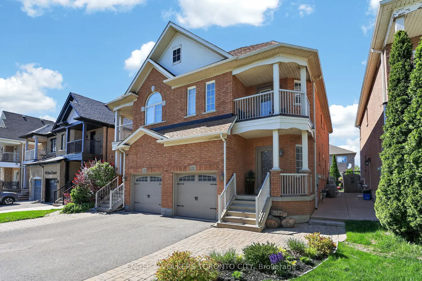 Two-story brick house with a double garage, white trim, and a second-story balcony on a sunny day.