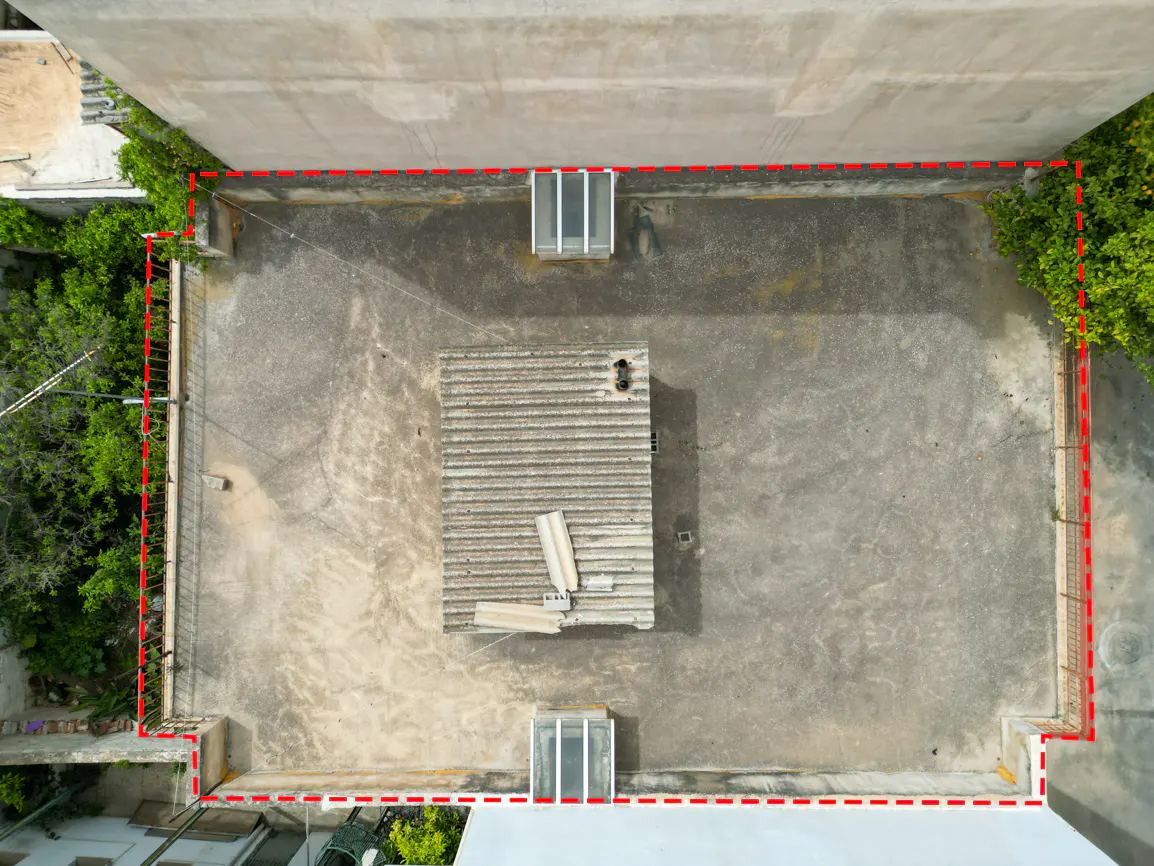 Aerial view of a flat rooftop, outlined in red, with a small structure and greenery.