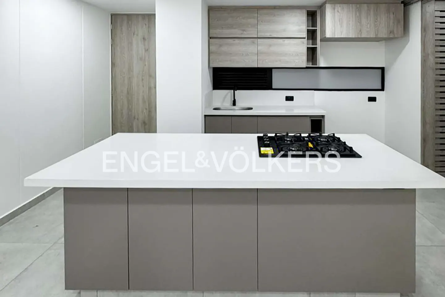 A modern kitchen with a white countertop island and a built-in gas stove. Gray cabinets and a sink are in the background.