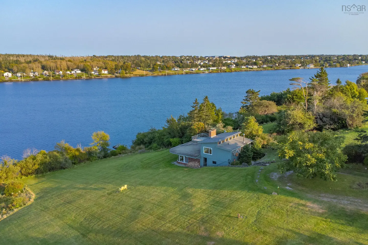 Aerial view of a blue house with a chimney on a green lawn near a blue river and trees.