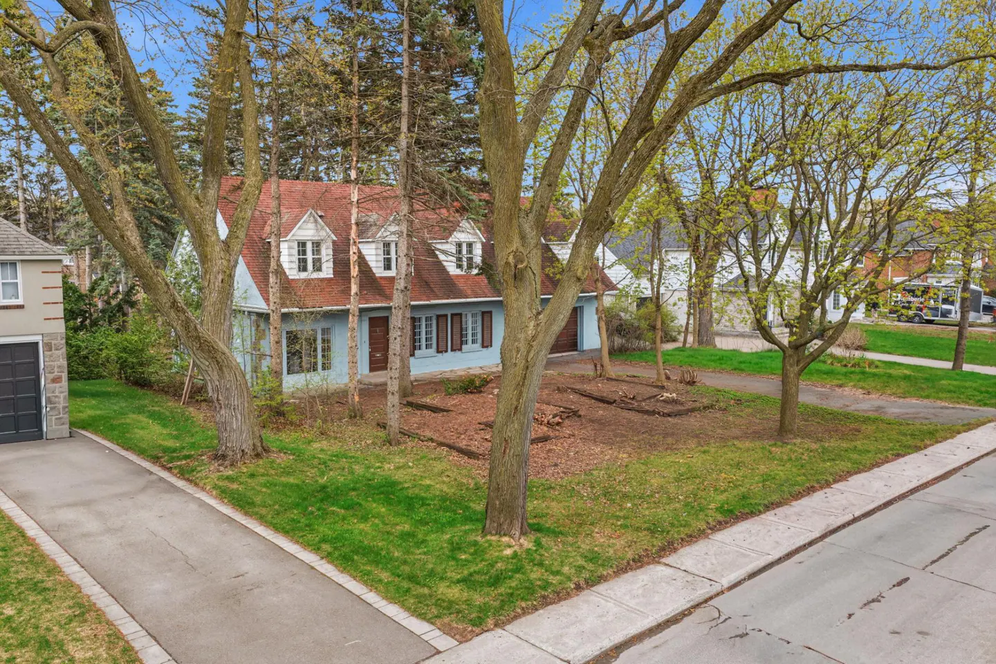 Two-story light blue house with a red roof, brown shutters, and white trim, surrounded by trees and a green lawn.