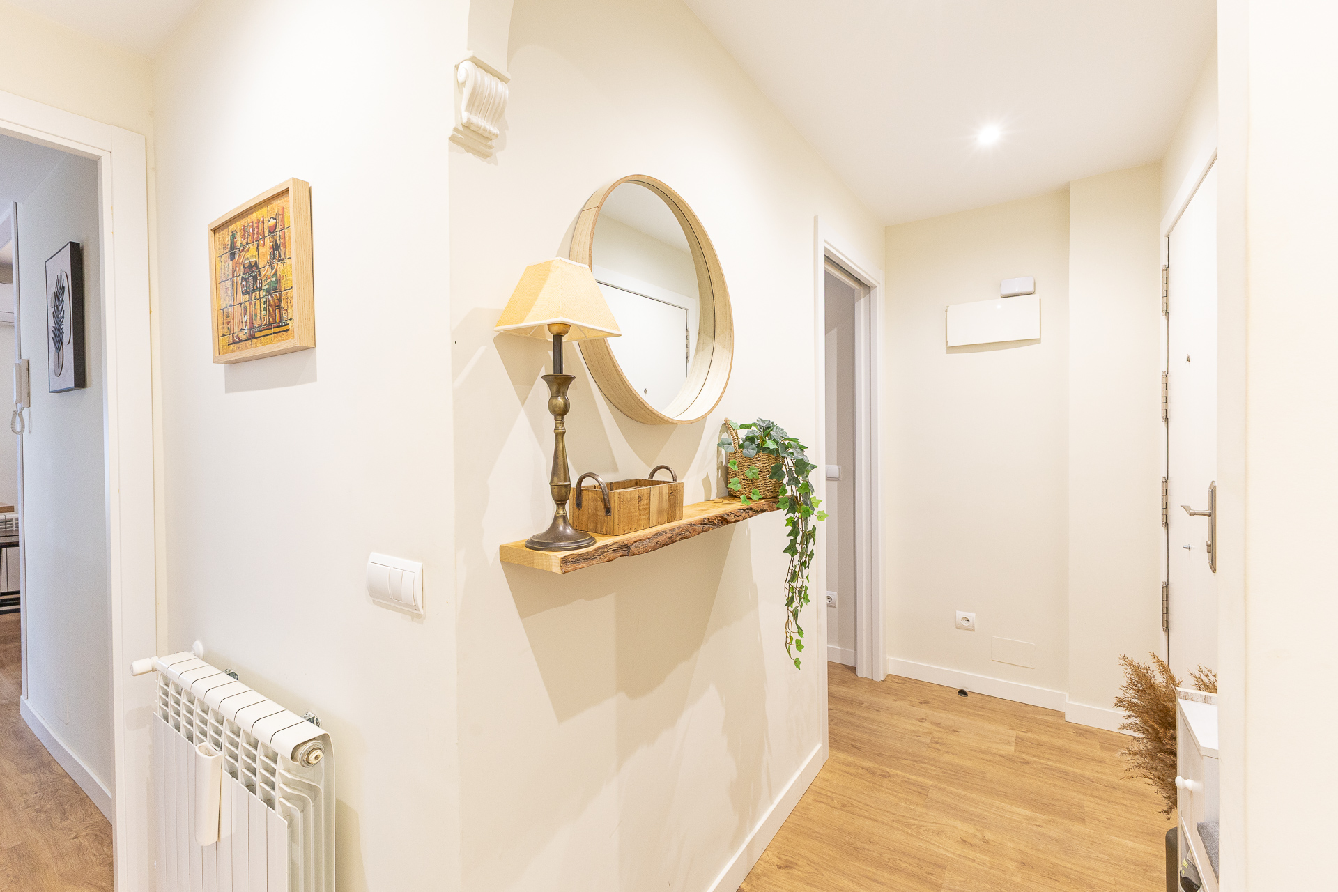 Bright hallway with wood floors, a live-edge shelf featuring a lamp and mirror, and a white radiator on the left wall.