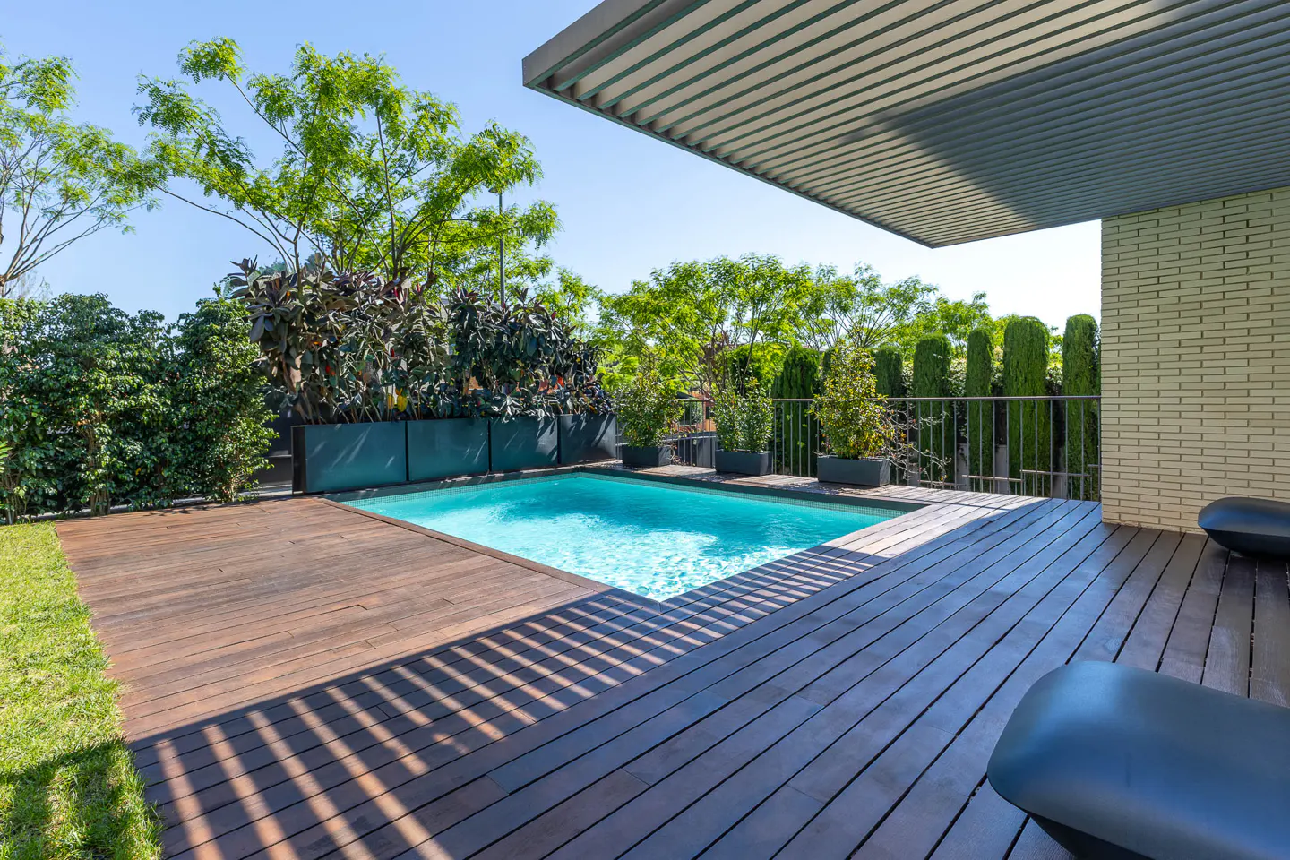 Rooftop pool with wooden deck, lounge chairs, and lush greenery under a modern pergola.