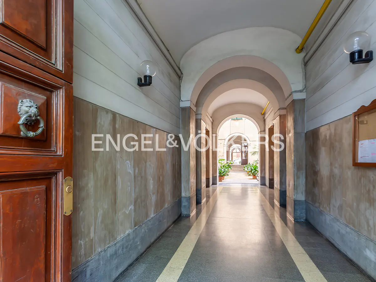 Arched hallway with marble walls and floor, leading to a bright doorway. A dark wood door with a lion knocker is on the left.